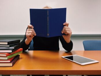 Frau versteckt sich hinter Lehrbuch