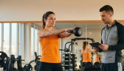 Ein Fitnesstrainer leitet eine Frau beim Hanteltraining im Fitnessstudio an.